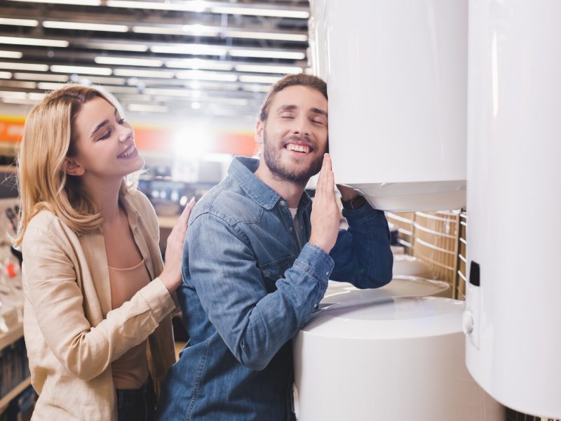 smiling boyfriend touching boiler and girlfriend looking at him in home appliance store
